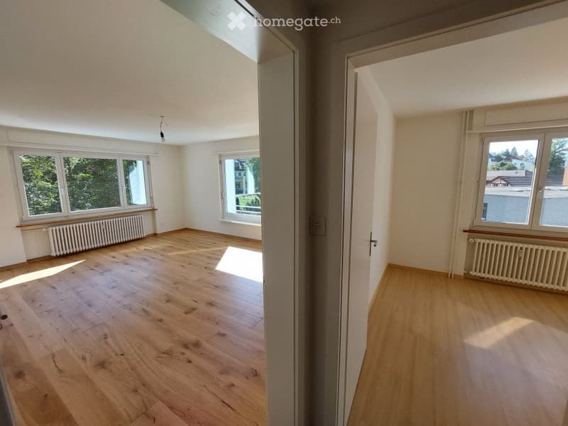 Empty room with wooden flooring, large windows, and radiators. No furniture or equipment present.