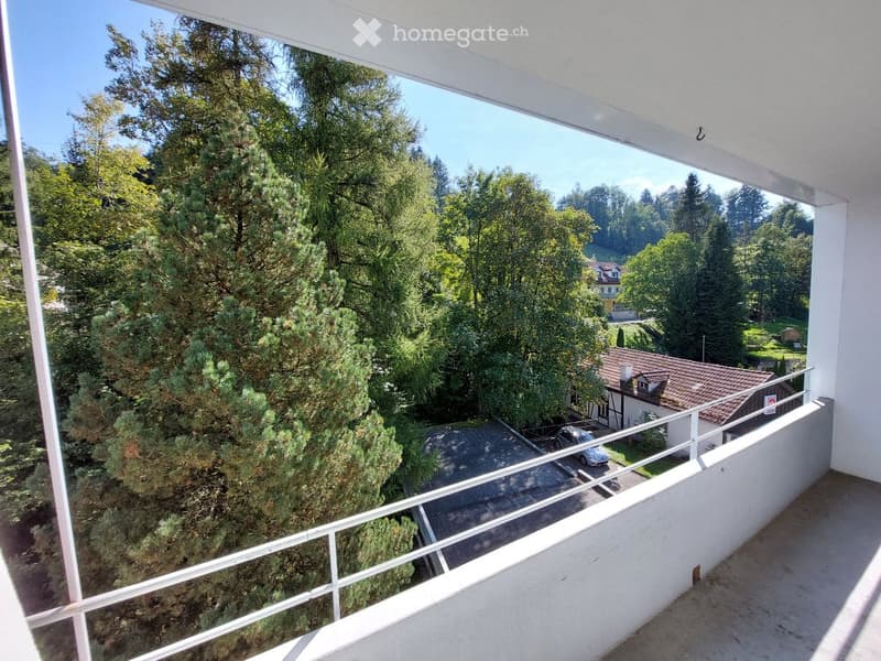 Balcony with a view of a lush green landscape, trees, and a house in the distance.
