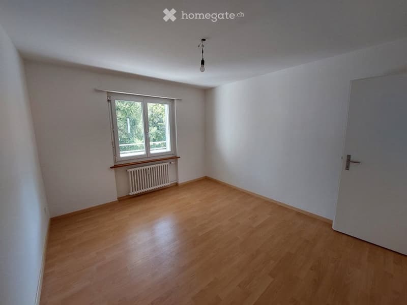 Empty room with wooden flooring, white walls, a single window with a radiator below, and a closed door.