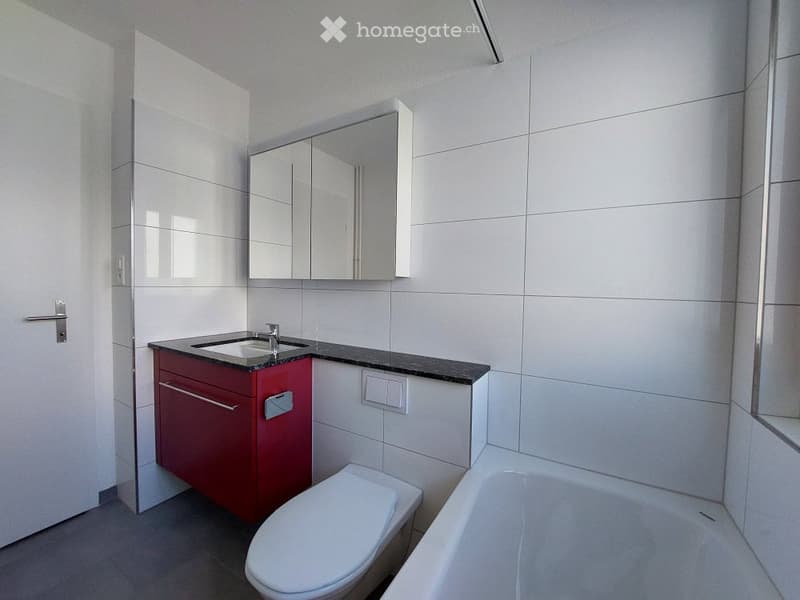 Modern bathroom with white tiles, red cabinet, sink, mirror, toilet, and bathtub.