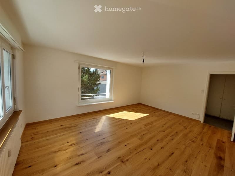 Empty room with wooden flooring, white walls, and large windows allowing natural light. No furniture or equipment present.