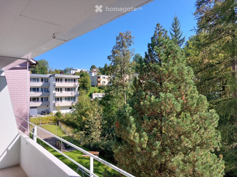 Balcony overlooking a green area with trees and residential buildings in the background.