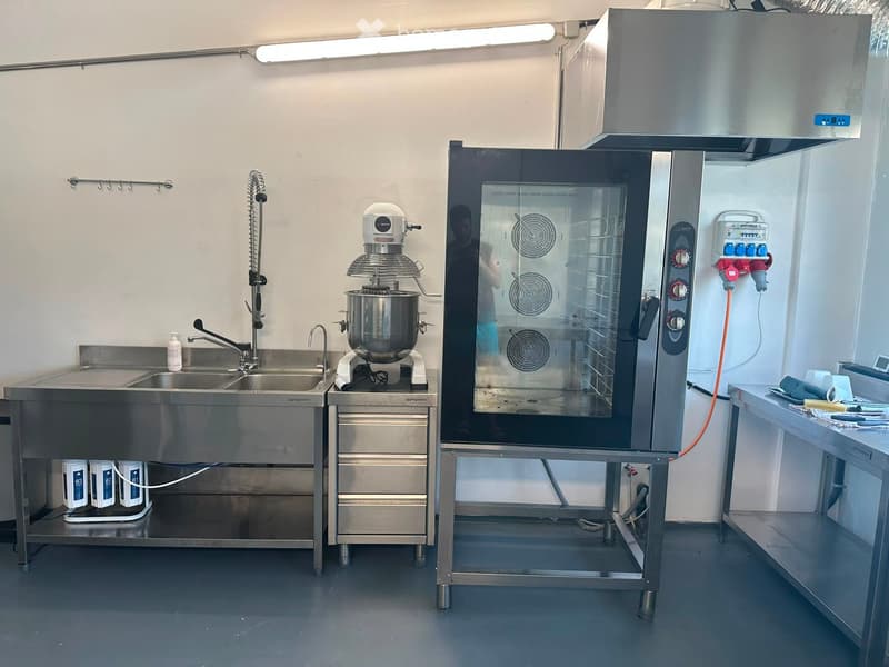 Commercial kitchen with stainless steel sink, mixer, oven, and storage units.