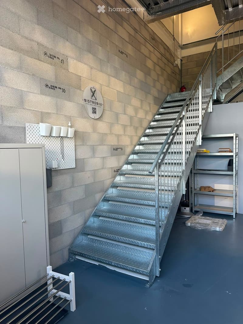 Metal staircase with handrail, grey walls, storage shelves, and a fire extinguisher visible in the background.