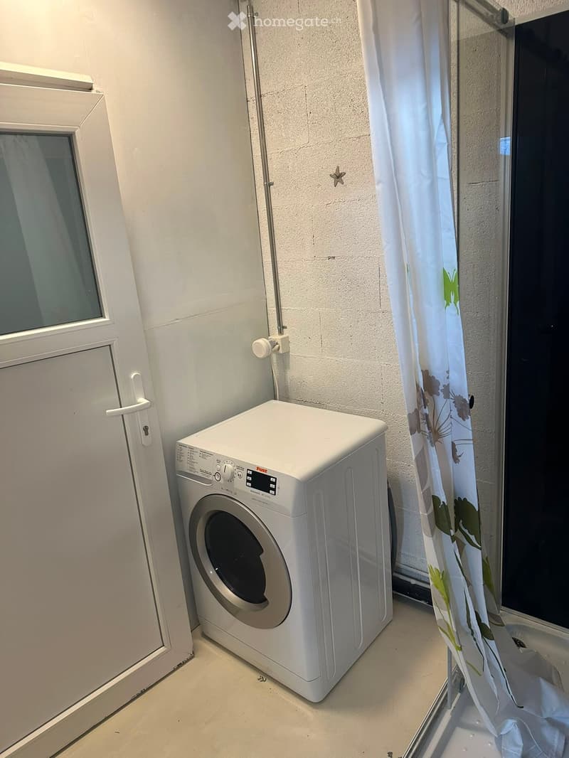 A compact bathroom with a white washing machine positioned near a window and a shower curtain with floral patterns.