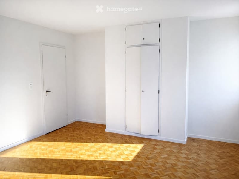 Empty room with white walls, wooden herringbone flooring, and built-in white cabinetry.