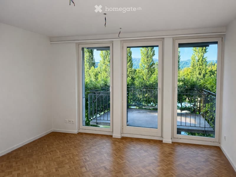 Empty room with wooden parquet flooring, white walls, and three large sliding glass doors leading to a balcony with a view of greenery and mountains.