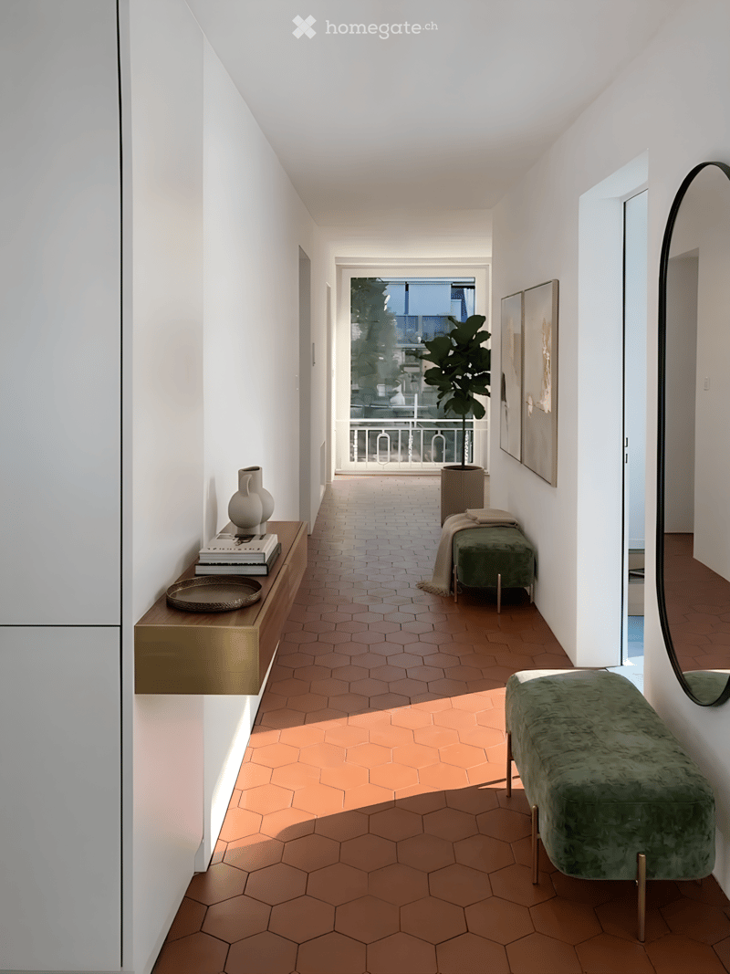 Modern hallway with hexagonal tile flooring in two tones, white walls, a green bench, a small table with books and a vase, and a large mirror on the wall.