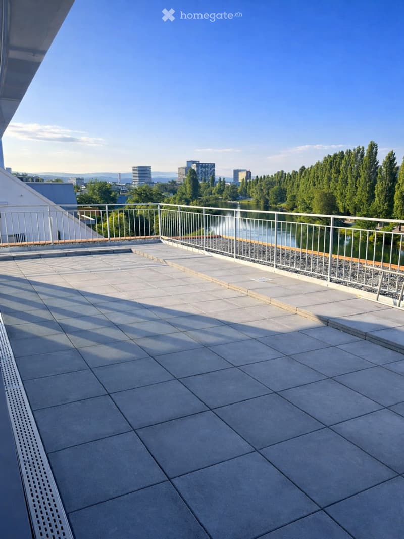 Rooftop terrace with tiled flooring, metal railing, and a view of a lake and city skyline.