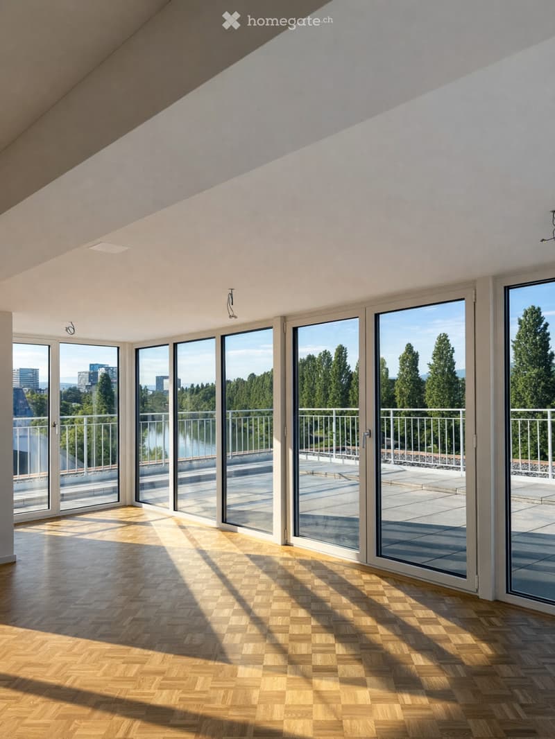 Bright, empty room with wooden flooring and large glass doors leading to a balcony with a scenic view of trees and a body of water.