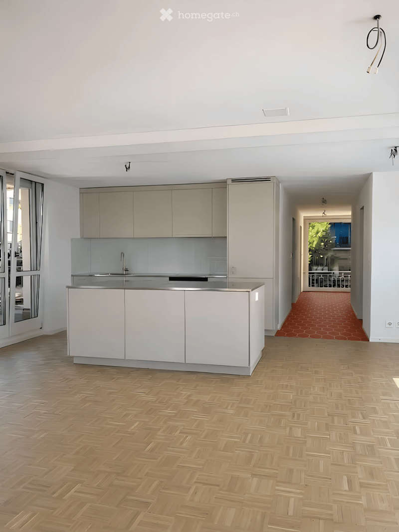Modern kitchen with white cabinets, a central island, and a sleek sink area. The floor is herringbone-patterned wood, and the space is open and bright.
