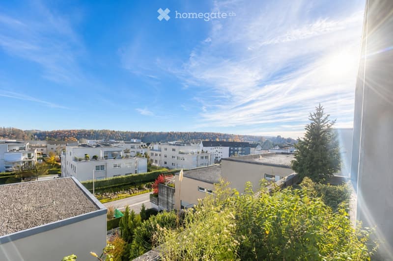 Balcony overlooking a residential area with modern apartment buildings, trees, and a clear blue sky.