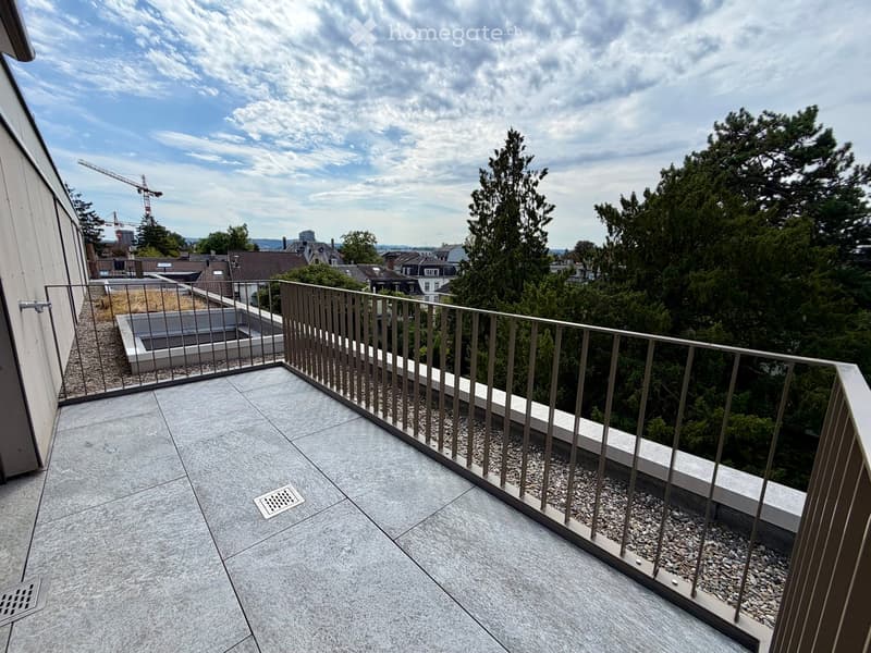 Modern balcony with grey tiled flooring, metal railing, and a view of trees and cityscape.