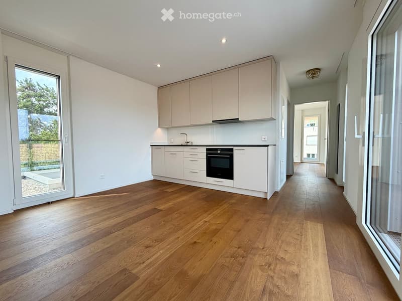 Modern kitchen with light-colored cabinets, a built-in oven, and a sleek faucet, featuring wooden flooring and large windows with a view of greenery.