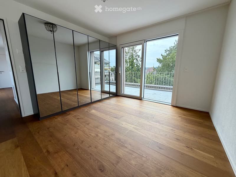 Empty room with wooden flooring, large mirrored wardrobe, and sliding glass doors leading to a balcony.