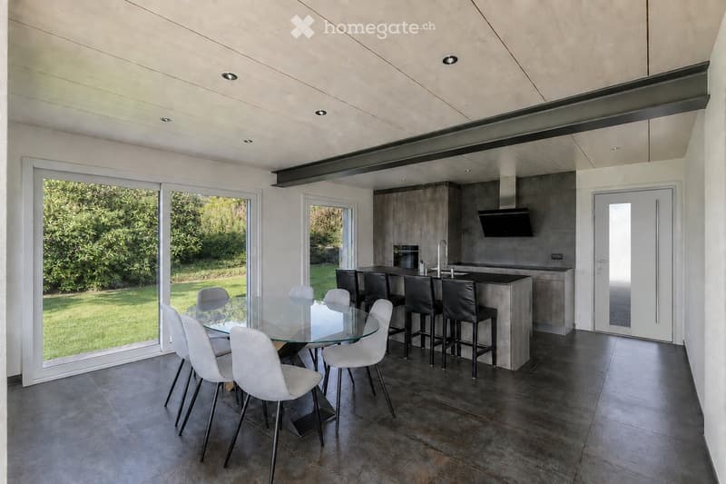 Modern open-plan kitchen and dining area with a glass dining table, white chairs, bar stools, and a kitchen island with cabinets and appliances.