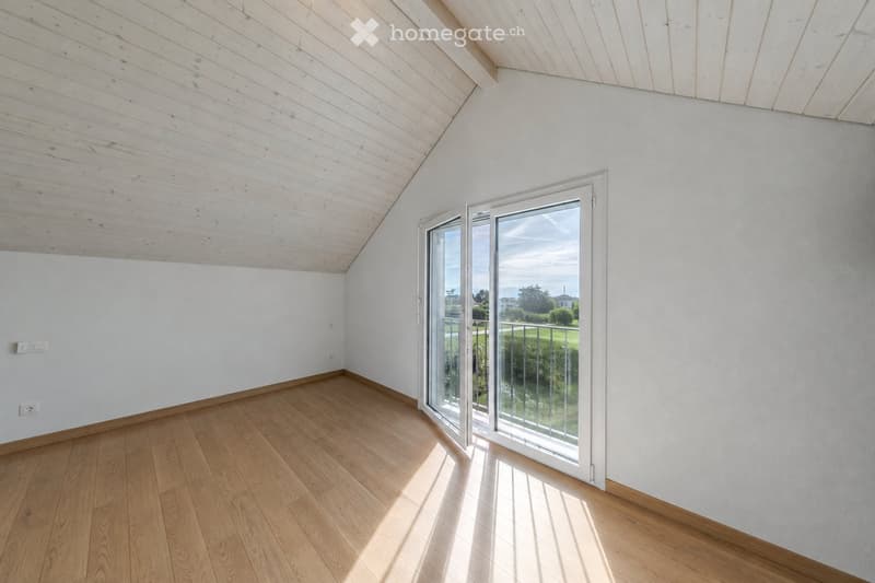 Bright, empty room with wooden flooring and white walls, featuring a large sliding glass door leading to a balcony with a view of greenery.