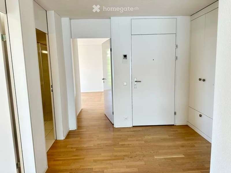 Empty hallway with wooden flooring, white walls, and white doors.
