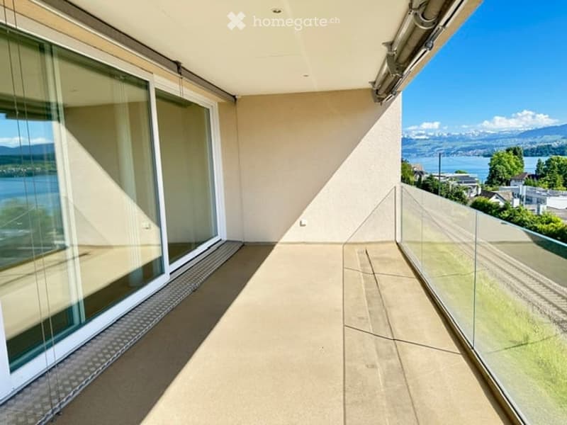 Modern balcony with large glass sliding doors, expansive ocean and mountain views, clean lines, and a spacious concrete floor.