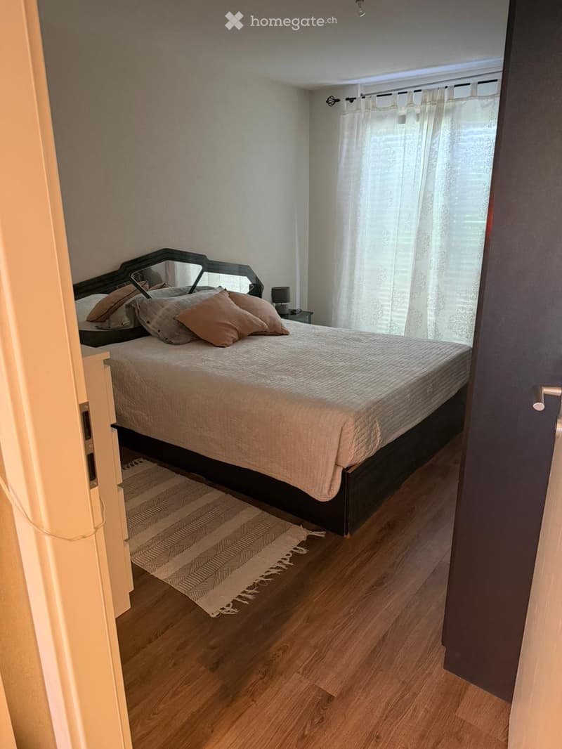 Cozy bedroom with a wooden bed, nightstand, lamp, and a patterned rug on the floor.