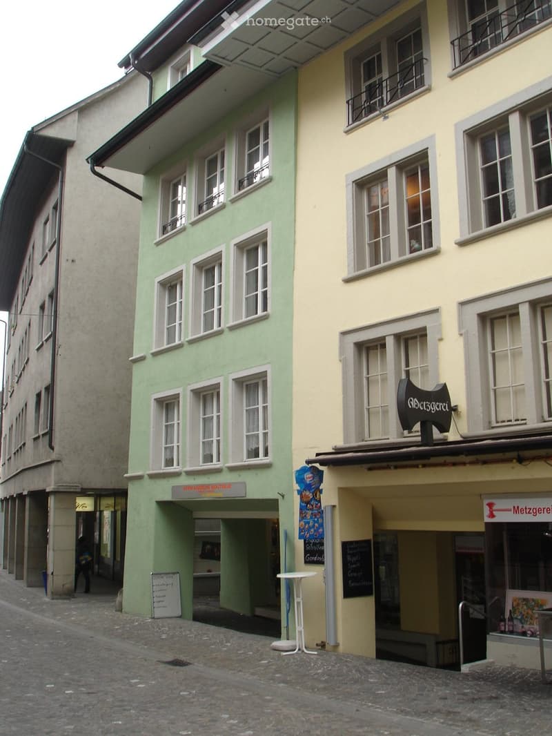 Two-story building with green and yellow facades, multiple windows, storefronts, and signage.