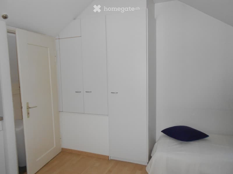 A small bedroom with a single bed, a dark pillow, a white wardrobe, and a wooden floor.