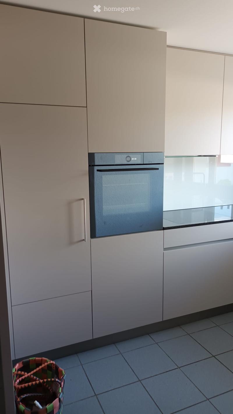 Modern kitchen with light-colored cabinets, a built-in oven, and tiled flooring.