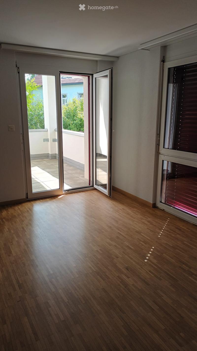 Empty room with wooden flooring, large sliding glass doors leading to a balcony, and natural light streaming in.
