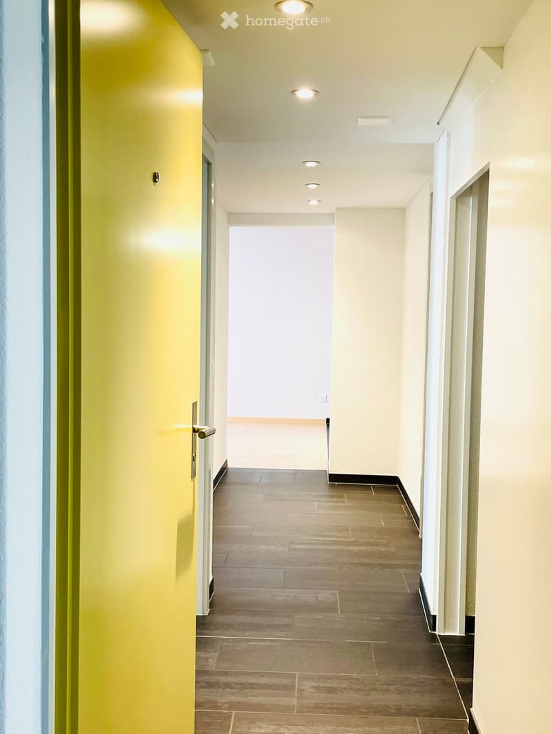 Empty hallway with yellow door, wooden floor, white walls, ceiling lights