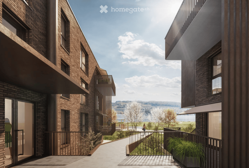Modern multi-story brick building with balconies overlooking a scenic landscape, featuring a pathway and greenery.