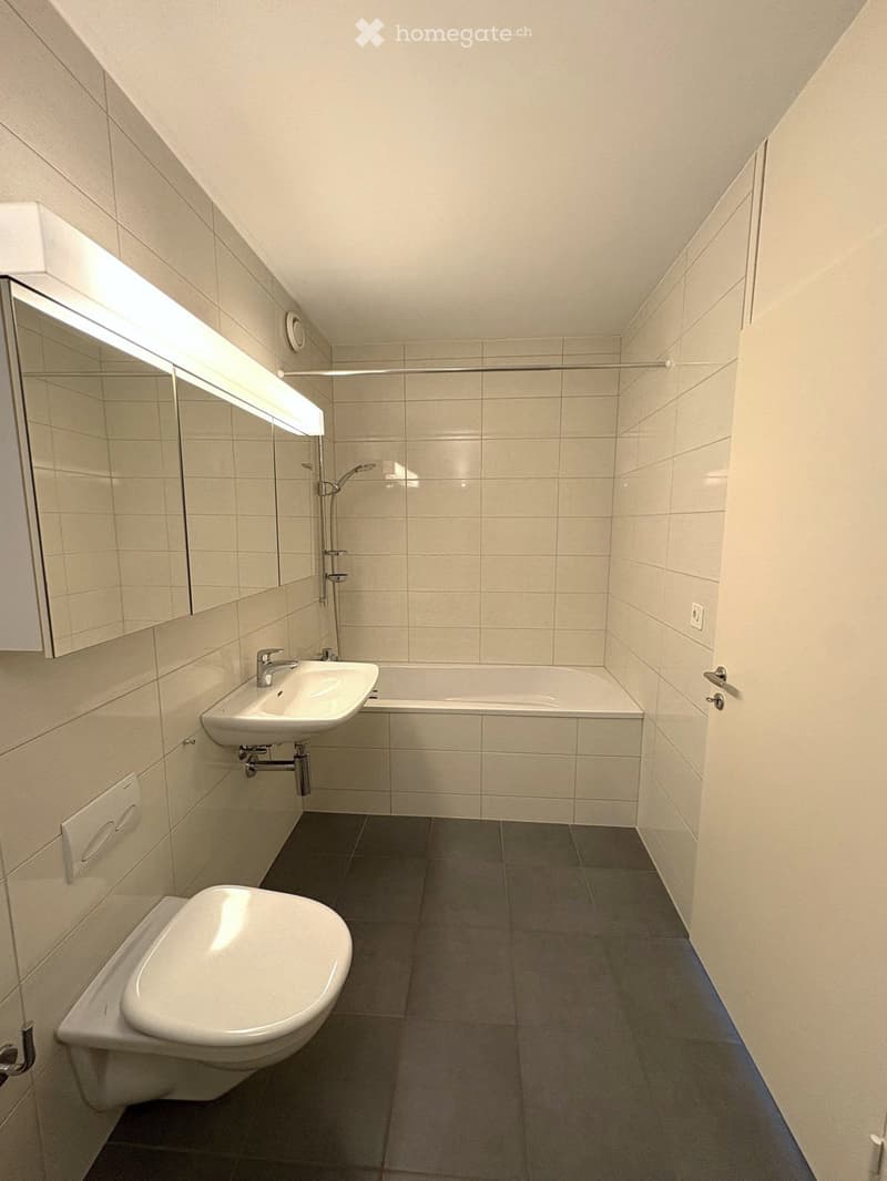 Modern bathroom with white tiles, a sink, bathtub, toilet, and a large mirror with built-in lighting.