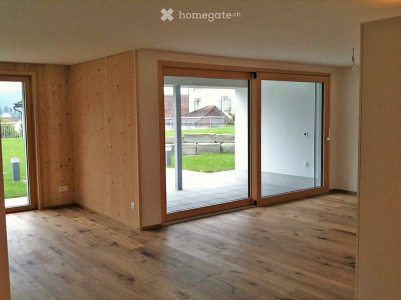 Empty room with wooden flooring, large sliding glass doors leading to a patio, and natural light from windows.