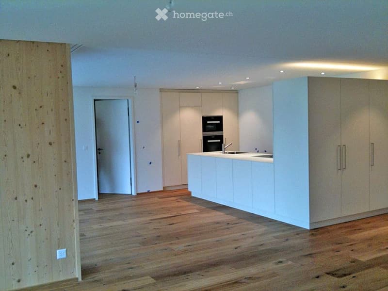 Modern kitchen with white cabinets, a central island, and wooden flooring.