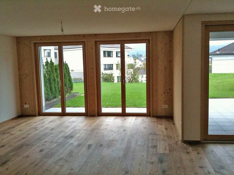 Empty room with wooden flooring and large sliding glass doors leading to a green outdoor area.