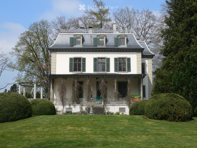 Two-story house with white siding, green shutters, grey roof, and a porch with columns and a decorative railing.