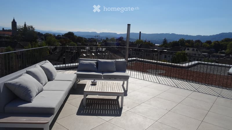 Modern rooftop terrace with white sofas, coffee table, and scenic city view.