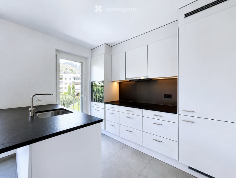 Modern kitchen with white cabinets, black countertops, stainless steel sink, and built-in oven. Features a large window with a scenic view.