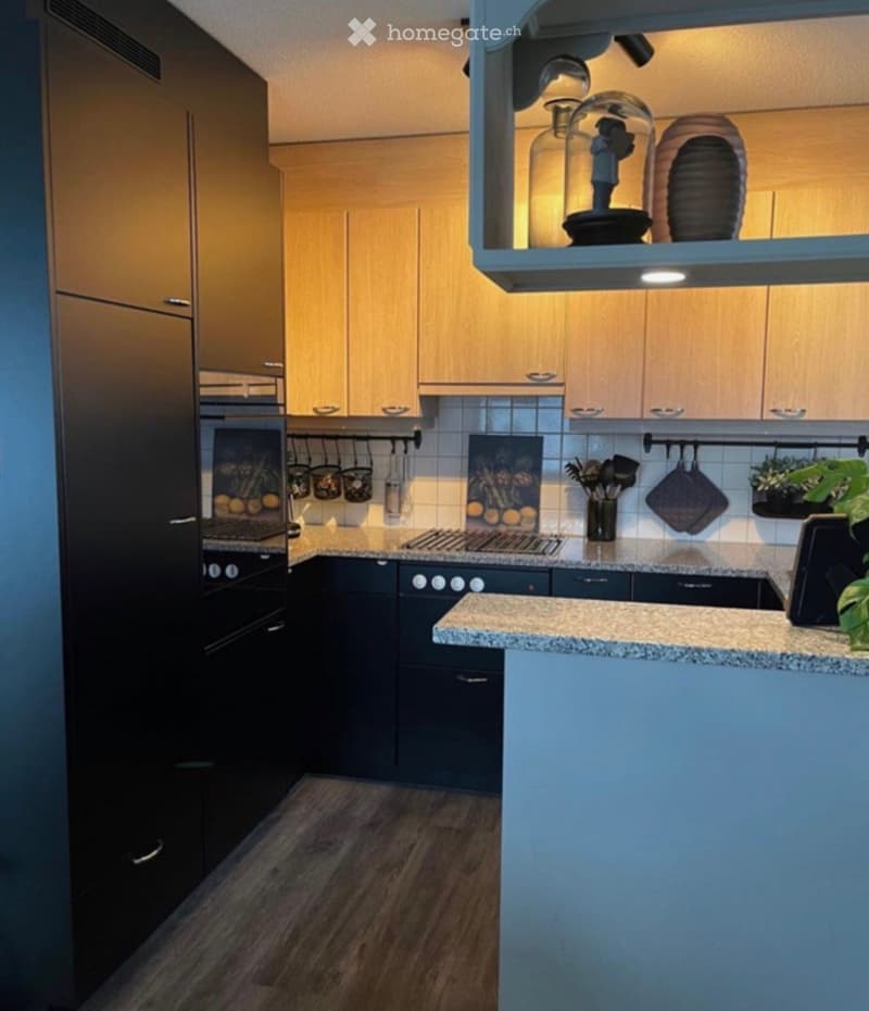 Modern kitchen with light wood cabinets, dark lower cabinets, granite countertop, stainless steel appliances, and decorative jars on a shelf.