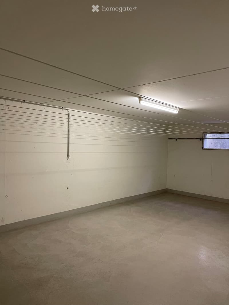 Empty garage with concrete floor, white walls, fluorescent lighting, and a small window at the far end.