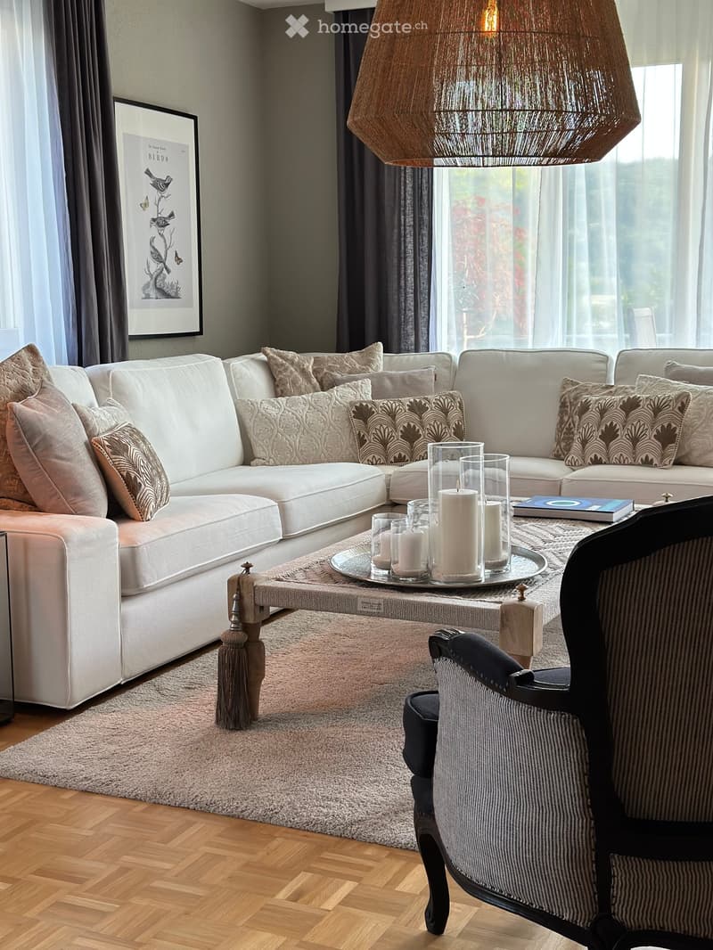 Modern living room with a white sectional sofa, patterned cushions, a coffee table with candles, a patterned rug, and a wooden floor.