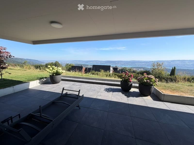 Modern balcony with expansive scenic view, tiled floor, lounge chairs, and potted plants.