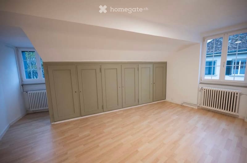 Empty room with wooden flooring, built-in cabinets, and large windows offering a view of the outside.