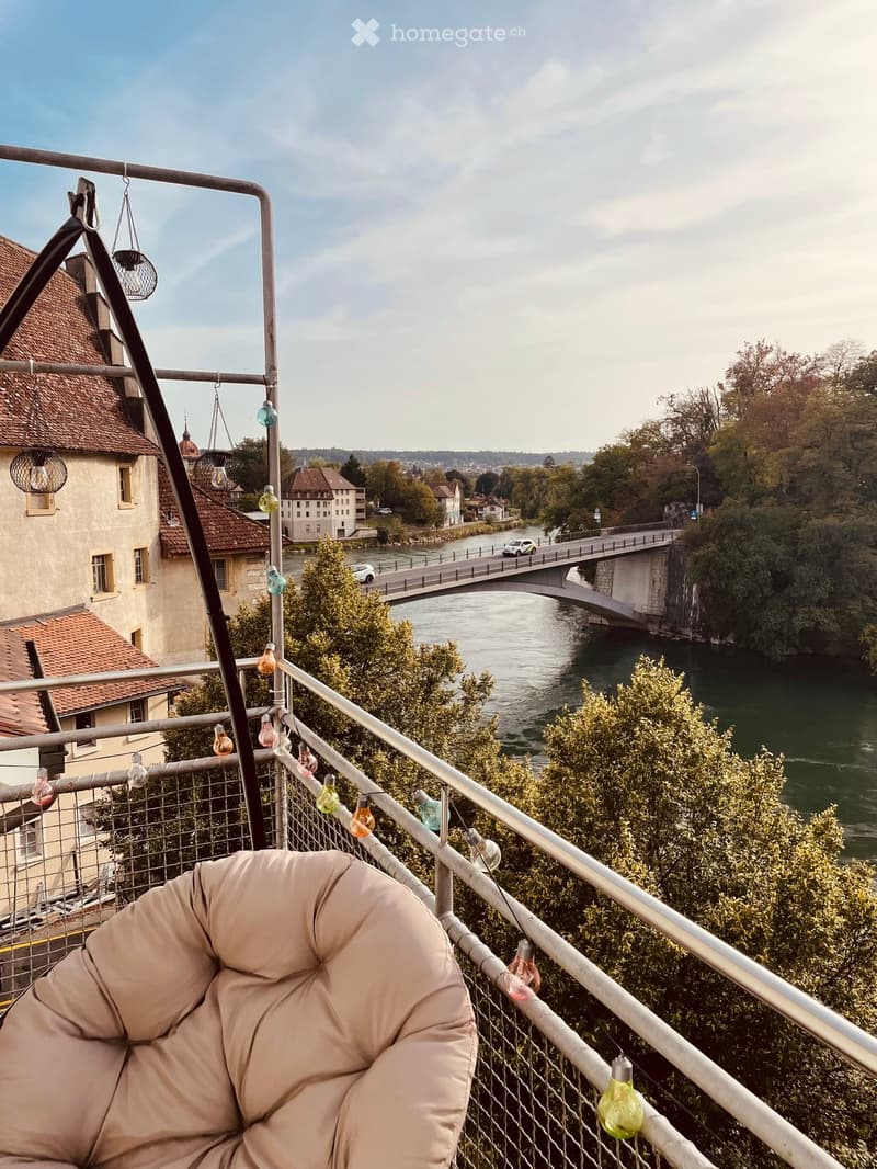 Balcony overlooking a river with a bridge, featuring a bean bag chair and string lights.