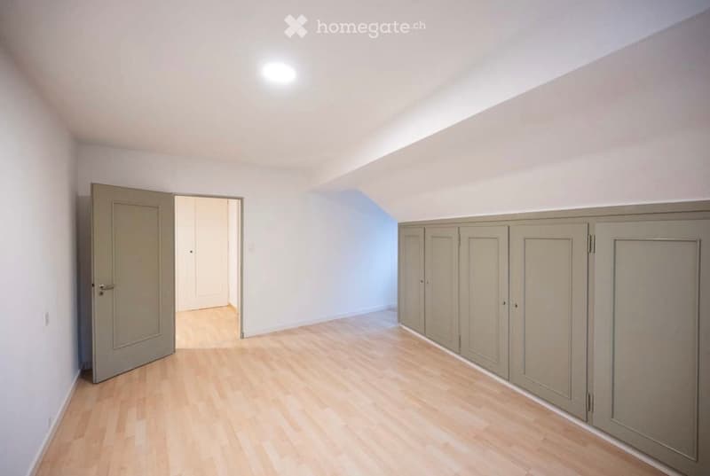 Empty room with light wooden flooring, white walls, built-in cabinets, and a door leading to another space.