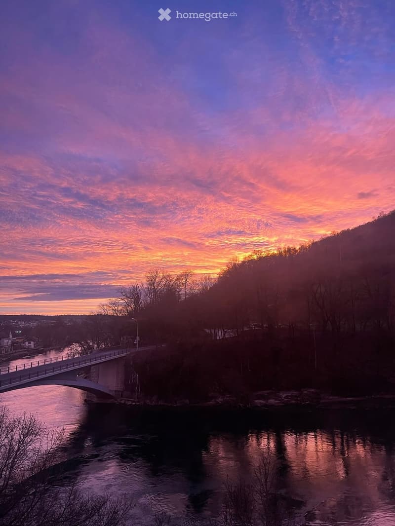 A scenic view of a river at sunset, with a bridge spanning the water and trees lining the banks.