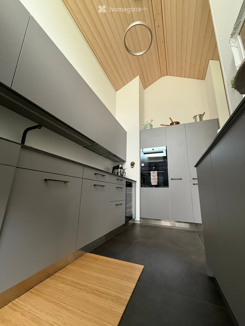 Modern kitchen with grey cabinets, dark tiled floor, and a wooden accent area. Features an oven, kitchen island, and various kitchen appliances.