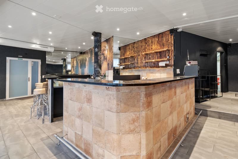 Modern bar area with a stone bar counter, wooden shelves, bar stools, and a door leading to another room.