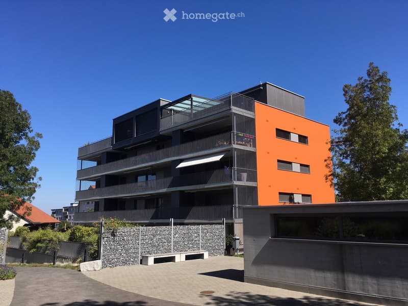 Modern multi-story residential building with orange and grey facade, balconies, and contemporary design.