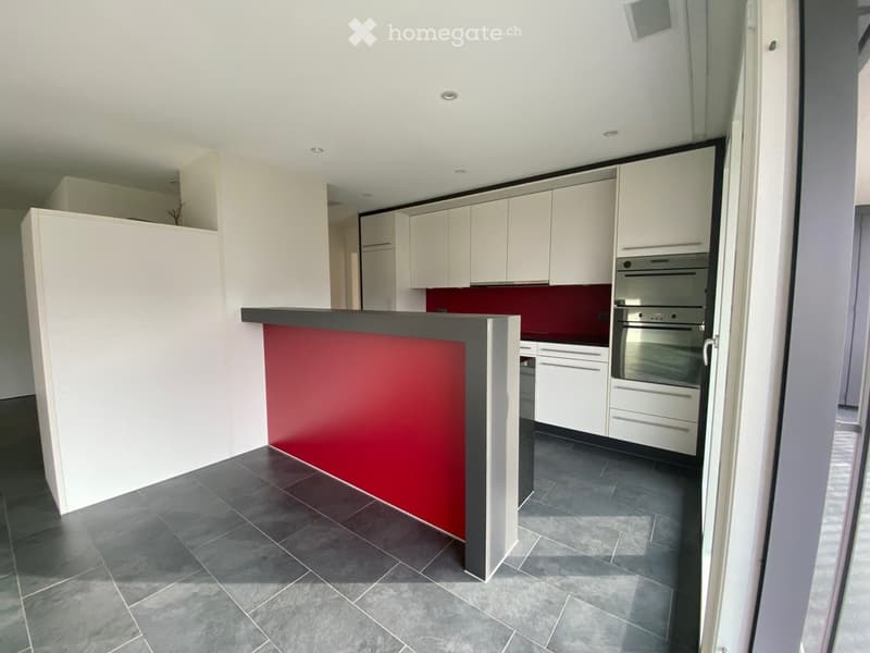 Modern kitchen with white cabinets, dark tiled floor, and a red accent wall behind the counter.
