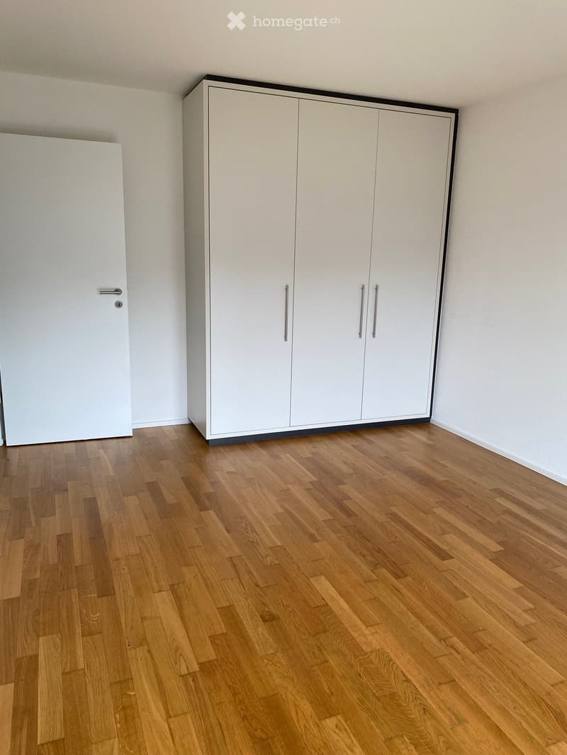 Empty room with light wooden flooring and white walls, featuring built-in white wardrobes with silver handles.